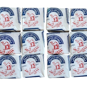 May include: A collection of twelve white soap bars, each wrapped in paper with blue and red text and a camel illustration. The soap bars are arranged in a grid pattern, showcasing the product's packaging and design.