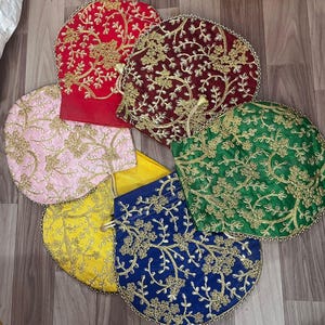 Può includere: Una collezione di sacchetti con coulisse ricamati, colorati. I sacchetti sono in vari colori, tra cui rosso, rosa, giallo, blu, verde e bordeaux. Ogni sacchetto presenta un'intricata ricamatura floreale dorata e un bordo di perline.