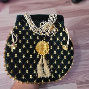 May include: A dark green velvet drawstring pouch featuring a quilted diamond pattern with gold sequins at each intersection. The bag includes a multi-strand white pearl handle, a central gold floral embellishment, and two beige tassels.