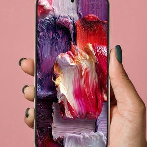 May include: A smartphone with a thin black bezel displaying a vibrant abstract digital wallpaper featuring thick, textured strokes of red, purple, white, and pink oil paint. The device has a centered front-facing camera lens at the top edge.