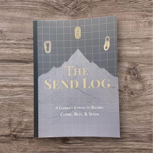 May include: A journal titled "The Send Log" for climbers, featuring a mountain graphic and climbing-related icons. The cover is gray with gold lettering and includes the text "A Climber's Journal to Record: Climbs, Beta, & Sends."