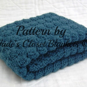 以下が含まれることがあります： テクスチャのあるパターンが施されたターコイズブルーのクロシェ編みブランケット。ブランケットは半分に折り畳まれており、「Pattern by Jade's Closet Blankets ©」というテキストが表示されています。