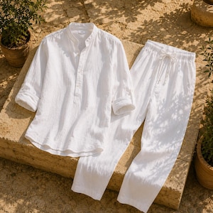 Pode incluir: Uma camisa branca de manga comprida com gola mandarim e carcela de bot&otilde;es parcial, combinada com cal&ccedil;as brancas a condizer com cintura el&aacute;stica e fecho de cord&atilde;o. O conjunto &eacute; feito de um tecido leve e texturizado.