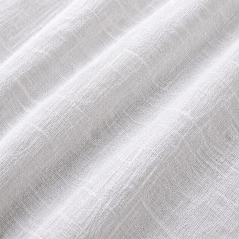 Pode incluir: Um tecido branco com uma trama vis&iacute;vel, solta e texturizada. O material apresenta uma qualidade semitransparente com um padr&atilde;o de grade criado pelos fios horizontais e verticais que se cruzam, exibindo dobras suaves e sombras leves.