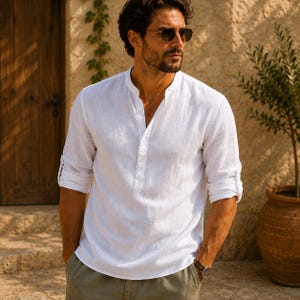 Pode incluir: Uma camisa branca de manga comprida com gola mandarim e carcela de bot&otilde;es parcial. A camisa apresenta mangas dobradas, um acabamento de tecido texturizado e um corte relaxado com um decote simples e linhas limpas.