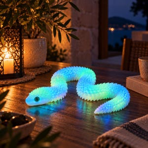 May include: A flexible, articulated snake toy featuring a textured, scale-like surface. The body emits a vibrant, glowing gradient of blue and green light, with dark, almond-shaped eyes positioned on the head. The toy is resting on a wooden surface.