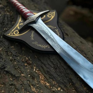 May include: A detailed shot of a sword with a silver blade and a red and white handle. The sword rests on a brown plaque with gold accents and inscriptions. The background is a textured wooden surface.