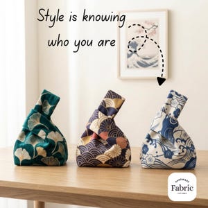 Può includere: Tre borse a nodo con manici in tessuto, caratterizzate da motivi distinti: una borsa verde scuro con foglie di ginkgo dorate, una blu navy con motivi circolari dorati e arancioni, e una crema con disegni floreali e onde blu. Testo: Style is knowing who you are.