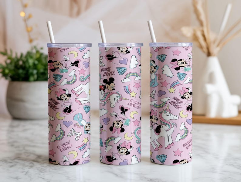 May include: Three pink insulated tumblers with white straws. The tumblers feature a repeating pattern of Minnie Mouse, unicorns, rainbows, stars, and diamonds. Text on the tumblers reads "100% REAL" and "UNICORN DREAM".