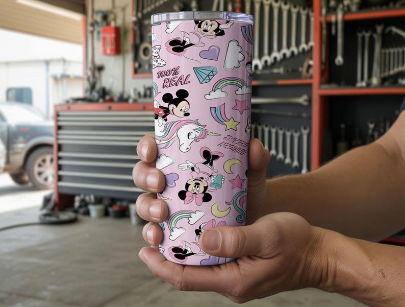 May include: A pink tumbler with a repeating pattern of Mickey and Minnie Mouse, unicorns, rainbows, and the text "100% REAL". The tumbler is cylindrical and appears to be made of stainless steel.