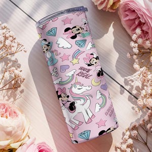May include: A pink tumbler featuring a repeating pattern of Minnie Mouse, unicorns, rainbows, diamonds, and stars. The words "100% REAL" are printed on the tumbler. The tumbler is surrounded by pink roses and white flowers.