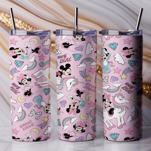 May include: Three pink insulated tumblers with a repeating pattern of Minnie Mouse, Mickey Mouse, rainbows, unicorns, and diamonds. Each tumbler has a silver straw and a lid. The text "100% REAL" and "UNICORN DREAMS" are also visible.