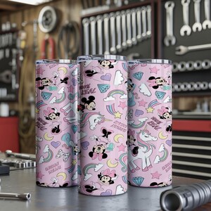 May include: Three pink insulated tumblers with a repeating pattern of Minnie Mouse, unicorns, rainbows, and diamonds. The tumblers have the text "100% REAL" and "UNICORN DREAMS". The tumblers are cylindrical and appear to be made of stainless steel.