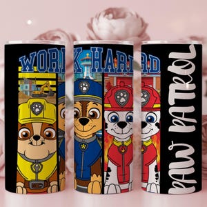 Puede incluir: Tres vasos negros con coloridos diseños de Paw Patrol. Un vaso presenta el texto "WORK HARD" con una escena de construcción. Los otros dos vasos tienen personajes de Paw Patrol y el texto "PAW PATROL" en escritura blanca.