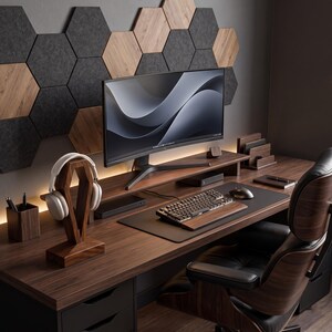 May include: A home office setup featuring a dark wood desk, a curved computer monitor, a mechanical keyboard with a wooden wrist rest, a black mouse pad, a wooden headphone stand with white headphones, and a wooden pen holder, all set against a wall with hexagonal panels.