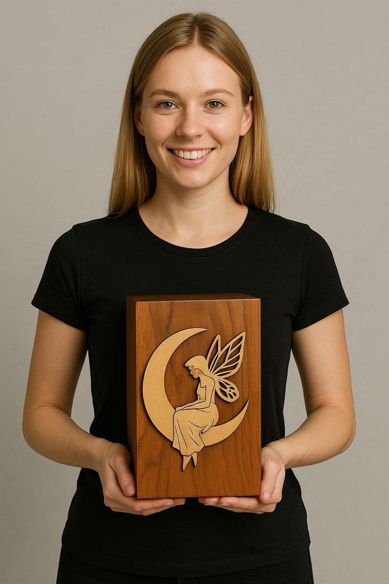 May include: A rectangular wooden box featuring a light-colored wood inlay of a fairy sitting on a crescent moon. The box is constructed from a medium-brown wood with a visible grain pattern, and the fairy figure is depicted in profile with wings.