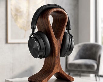 May include: A pair of black over-ear headphones resting on a curved, dark brown wooden stand. The headphones feature a smooth, matte black finish on the ear cups and a padded headband, while the stand has a distinct, arched, organic shape.