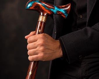May include: A walking cane featuring a dark brown wood shaft with inlaid diamond and circular brass accents. The T-shaped handle is crafted from dark wood with a swirling, bright turquoise resin inlay and a decorative brass collar.