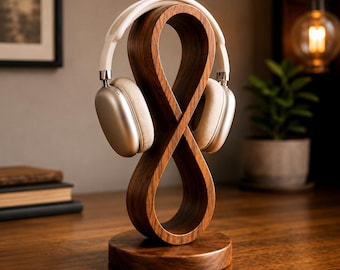 May include: A dark brown wooden headphone stand featuring a continuous infinity loop design mounted on a circular base. A pair of white over-ear headphones with silver accents rests securely on the top curve of the wooden structure.