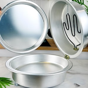May include: Three aluminum baking pans. One is a round lid, another is a round pan with a heating element, and the third is a round pan with small feet. The pans are silver and appear to be new.