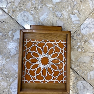 May include: A rectangular wooden tray with a geometric tile insert. The tile features a white starburst pattern on an orange background. The tray has a natural wood finish and small handles.