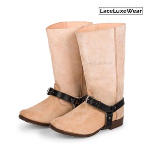 Puede incluir: Un par de botas de ante beige con correas y hebillas de cuero negro. Las botas tienen una caña alta y una puntera redondeada. La marca "LaceLuxeWear" es visible en la esquina superior derecha.