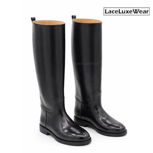 May include: Two black leather riding boots with a high, knee-length design. The boots have a polished, shiny appearance and a traditional style. The soles are flat. The brand name "LaceLuxeWear" is visible in the upper right corner.