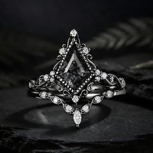 May include: A black ring set with a large, kite-shaped, dark gemstone. The ring is adorned with small, clear accent stones and detailed metalwork. A matching band with a curved design and small stones is also included.