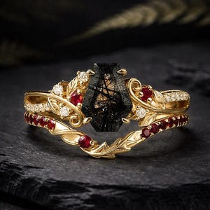 以下が含まれることがあります： 大きな黒いファセット宝石を中央に配した、ゴールドカラーのリングセット。リングは、小さな赤い宝石と透明なアクセントストーンで飾られ、葉のようなデザインにセットされています。セットには、お揃いのバンドが含まれています。