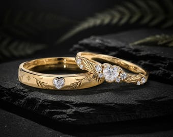 May include: Two gold rings featuring heart-shaped stones and leaf-like engravings. One ring has a central heart-shaped stone flanked by smaller round stones and leaf details, while the other is a band with a small heart stone and star accents.