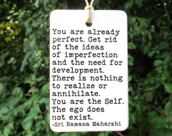 May include: White ceramic ornament with a black and white quote by Sri Ramana Maharshi: "You are already perfect. Get rid of the ideas of imperfection and the need for development. There is nothing to realize or annihilate. You are the Self. The ego does not exist."
