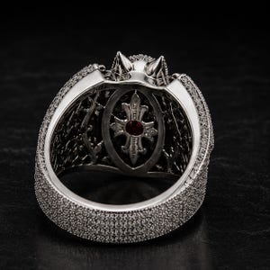 Side angle closeup of gothic bat wing ring with large red ruby center stone, black gemstone accents, and detailed silver pave setting. Luxury fantasy statement ring inspired by vampire and dragon themes, gothic jewelry for women and men, Halloween ring, dark aesthetic accessory, alternative fashion jewelry, biker ring, cosplay accessory, unique gothic engagement ring, handmade fantasy cocktail ring with bold dramatic design.