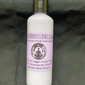 May include: A white bottle with a black cap and a lavender label. The label reads "Earthbound Calm" and lists ingredients like lavender mica powder. The bottle contains a liquid product, likely a lotion or oil.
