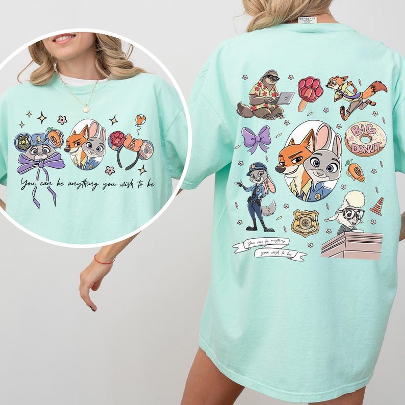 May include: A light teal t-shirt featuring cartoon characters and the text "You can be anything you wish to be." The front of the shirt has a circular design with characters. The back has a larger design with more characters and a donut.