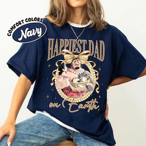 K&ouml;nnte beinhalten: Marineblaues T-Shirt mit goldenem Text "Happiest Dad on Earth". Das Shirt zeigt eine Cartoon-Illustration eines Mannes, der ein Kind h&auml;lt. Die Worte "Comfort Colors" und "Navy" befinden sich in einem wei&szlig;en Oval.