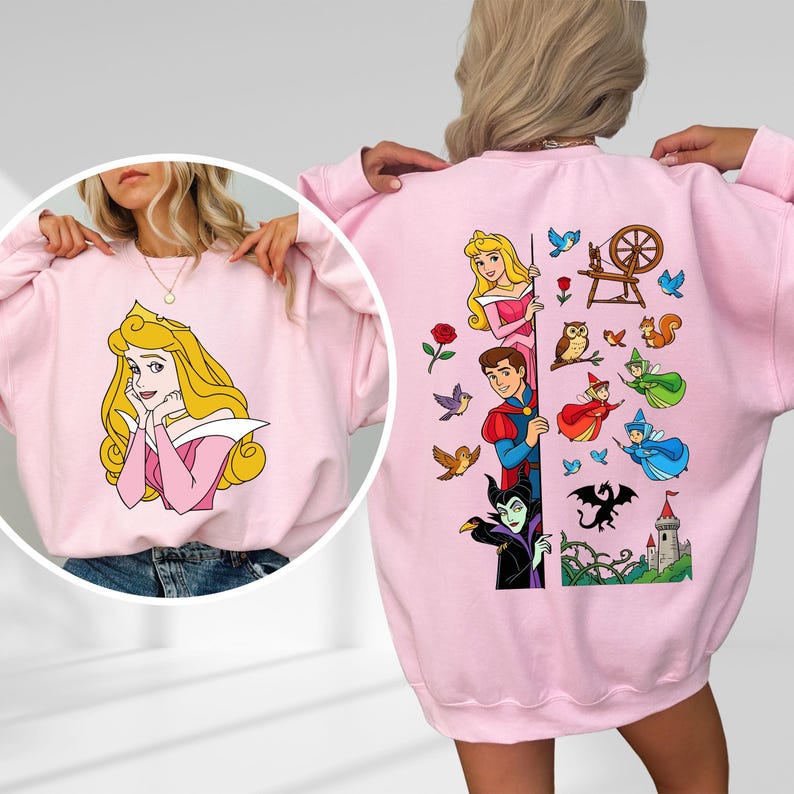 Puede incluir: Sudadera rosa claro con una ilustraci&oacute;n de dibujos animados de una princesa en la parte delantera. La parte posterior de la sudadera tiene un gr&aacute;fico m&aacute;s grande con personajes y elementos adicionales de la misma pel&iacute;cula animada. El dise&ntilde;o incluye un castillo, un drag&oacute;n y otros personajes.