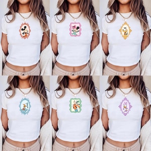 May include: White t-shirts with various cartoon character portraits in decorative frames. The characters include Mickey Mouse, Minnie Mouse, Goofy, Donald Duck, and Daisy Duck. Each shirt features a different character design.