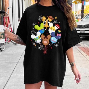 May include: A black t-shirt featuring a graphic print of multiple balloons shaped like mouse ears, each decorated to resemble characters including Buzz Lightyear, Woody, Jessie, Bullseye, and Bo Peep, with their names written in script nearby.