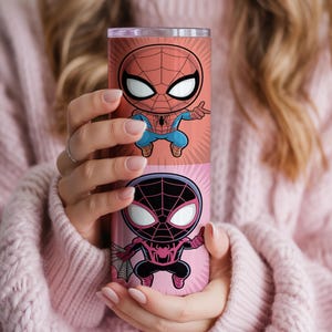May include: A cylindrical tumbler featuring two cartoon Spider-Man designs. The top design is red and blue, while the bottom is black and pink. The tumbler is held against a pink sweater.