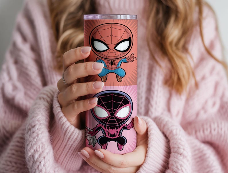 May include: A cylindrical tumbler featuring two cartoon Spider-Man designs. The top design is red and blue, while the bottom is black and pink. The tumbler is held against a pink sweater.