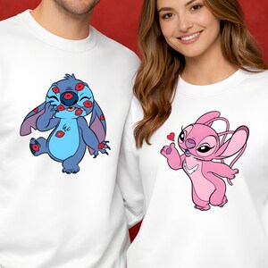 Puede incluir: Sudaderas blancas con personajes de dibujos animados. Una sudadera tiene un personaje azul con detalles rojos, la otra un personaje rosa. El fondo incluye globos en forma de coraz&oacute;n y luces de cadena, creando un ambiente festivo.