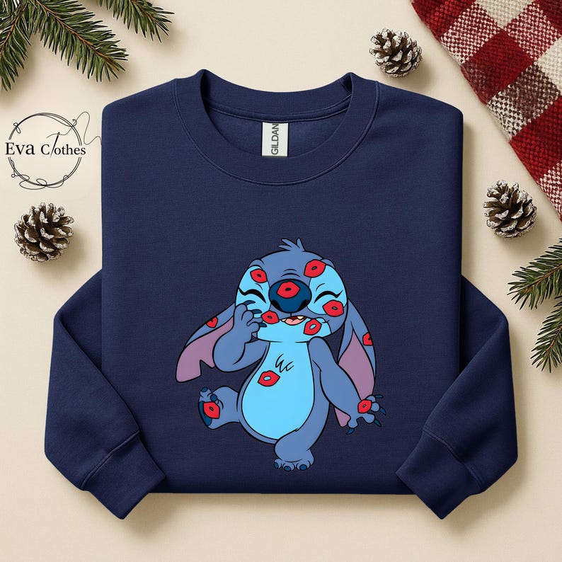 Puede incluir: Sudadera azul marino con un personaje de dibujos animados cubierto de marcas de besos rojos. El personaje es azul con orejas grandes y una expresi&oacute;n juguetona. La sudadera tiene cuello redondo y la marca "Gildan" es visible.