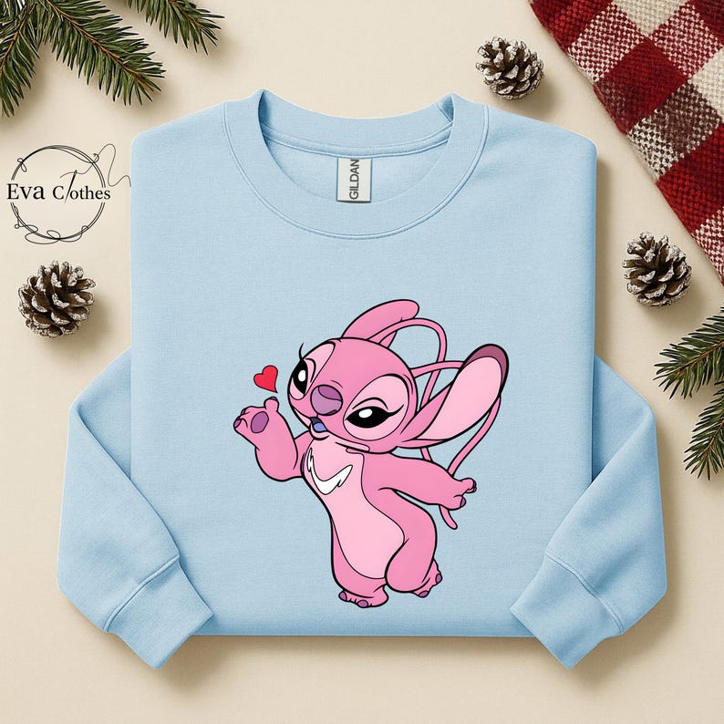 Puede incluir: Sudadera azul claro con un personaje de dibujos animados rosa sosteniendo un coraz&oacute;n rojo. El personaje tiene orejas grandes y una expresi&oacute;n amigable. La sudadera tiene mangas largas y cuello redondo. La etiqueta de la marca "Gildan" es visible.