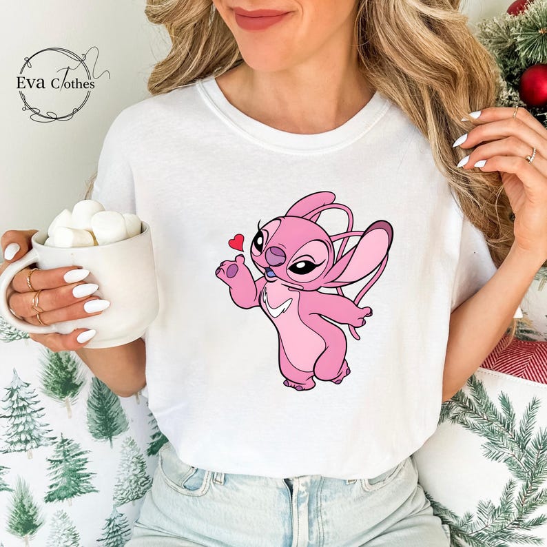 Puede incluir: Camiseta blanca con un personaje de dibujos animados rosa sosteniendo un coraz&oacute;n. El personaje tiene orejas grandes y es rosa. La camiseta tiene el texto "Eva Clothes" en cursiva.