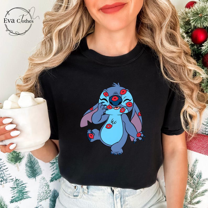 Puede incluir: Camiseta negra con un personaje de dibujos animados azul, con orejas grandes y vientre azul claro. El personaje est&aacute; cubierto de huellas de labios rojos. La camiseta tiene el logo de Eva Clothes en la esquina superior izquierda.