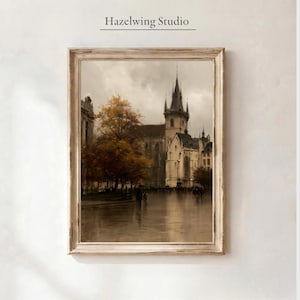 May include: A framed wall art print titled Hazelwing Studio featuring a sepia-toned cityscape of a gothic church with a tall spire, a large tree with golden autumn leaves, and a wet cobblestone square with silhouettes of people walking in the rain.