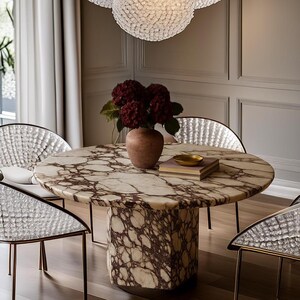 May include: A circular marble dining table with a brown and white pattern, supported by a matching pedestal base. The table is surrounded by four chairs with silver textured backs and thin gold legs. A vase of red flowers sits on the table, along with a small gold bowl.