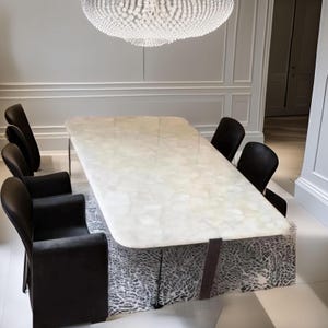May include: A contemporary dining set with a rectangular table, featuring a marble-effect top and dark legs, surrounded by six black chairs. The table sits on a patterned base. An elaborate chandelier hangs above.