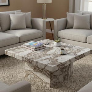 May include: A square coffee table with a marble-effect surface, in shades of white and brown. The table is in front of two light-coloured sofas. Books, a small plant, and a cup of coffee are on the table. The table is approximately 100 cm square.