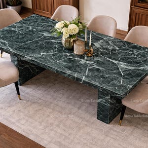 May include: A dark green marble dining table with white veining, supported by two solid pedestals. The table is surrounded by six beige upholstered chairs. A floral arrangement and candles are placed on the table. Table dimensions are approximately 200cm x 100cm.